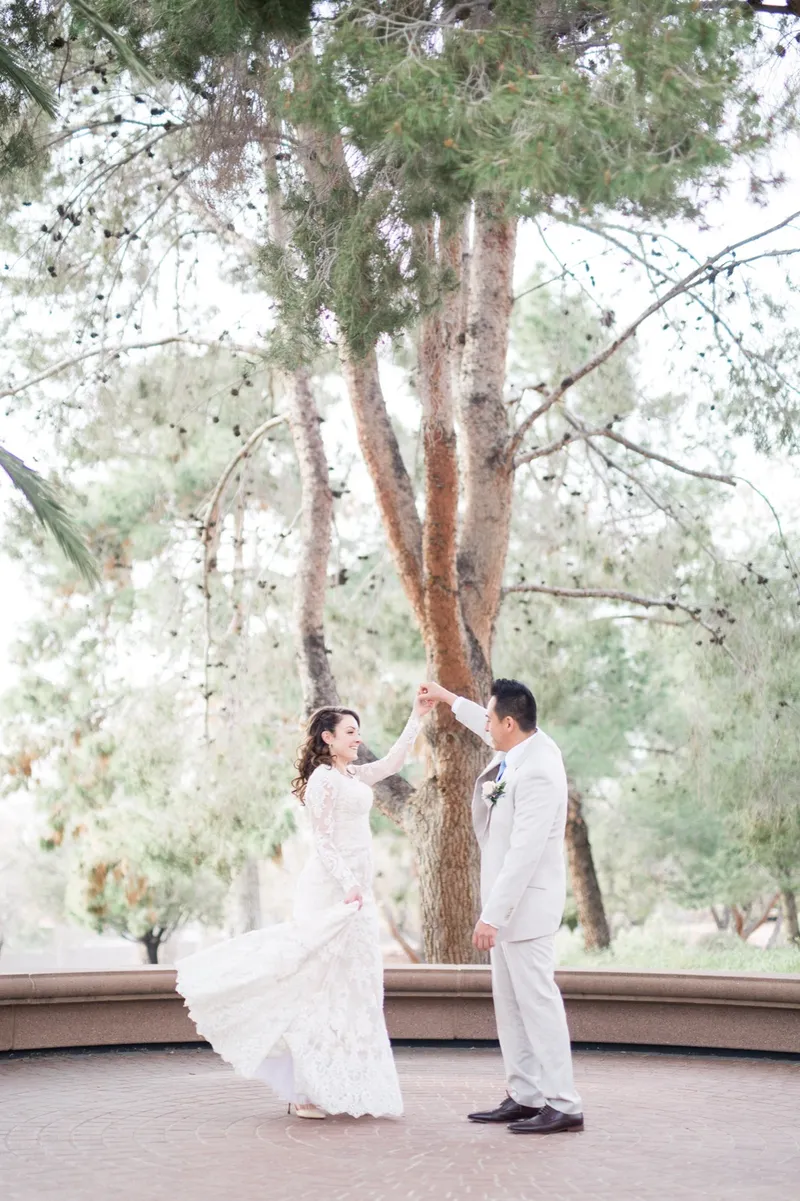 The groom lifting the bride's hand to turn her under the trees, her lace train swinging out behind