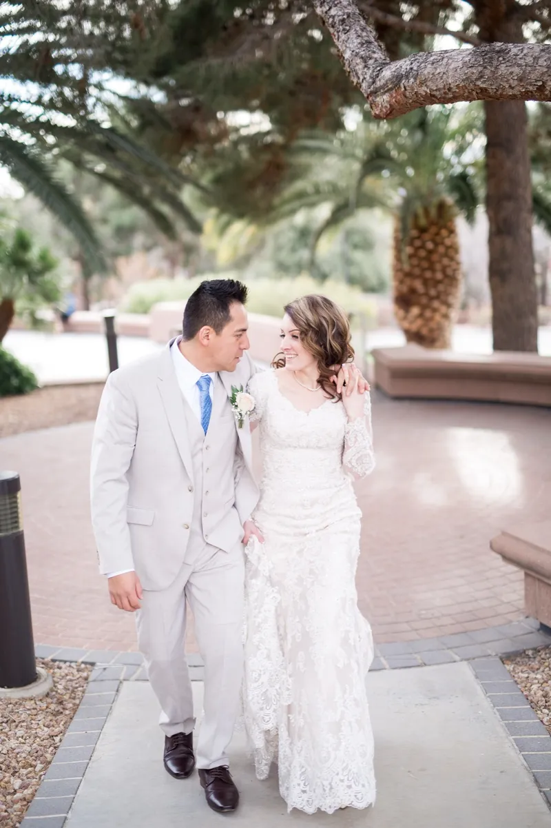 The couple walking a brick path together, the groom in a light tan suit and a blue tie