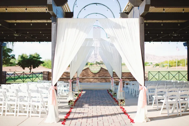Wider view of the same patio ceremony set with white chairs on both sides of the red petal aisle and the course beyond