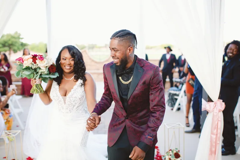 Couple walking back up the aisle hand in hand, the bride raising her red and white bouquet over her head