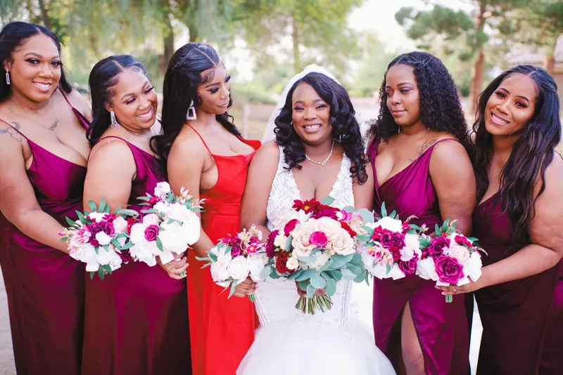 Bride surrounded by her bridesmaids in burgundy and red, all of them holding white and red bouquets