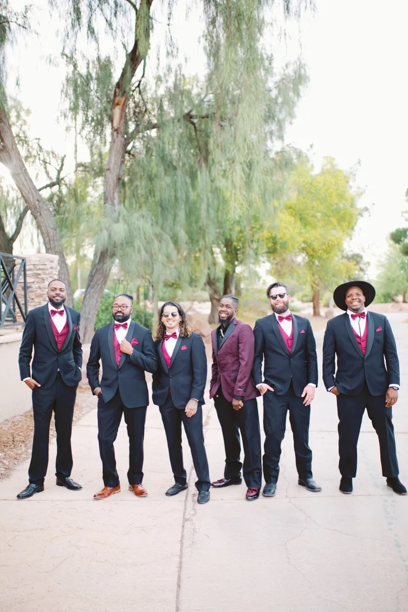 Groom and his groomsmen lined up in black suits with burgundy vests and bow ties