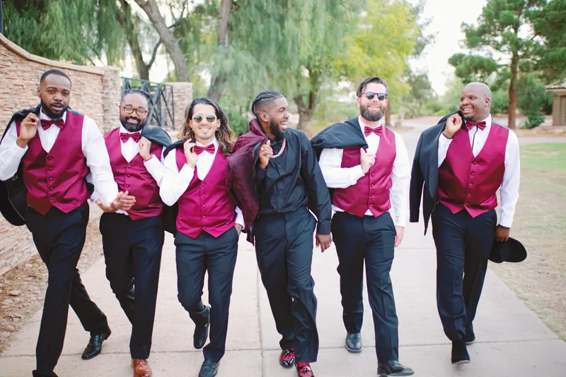 Groomsmen walking the cart path toward the camera in burgundy vests with their jackets over their shoulders