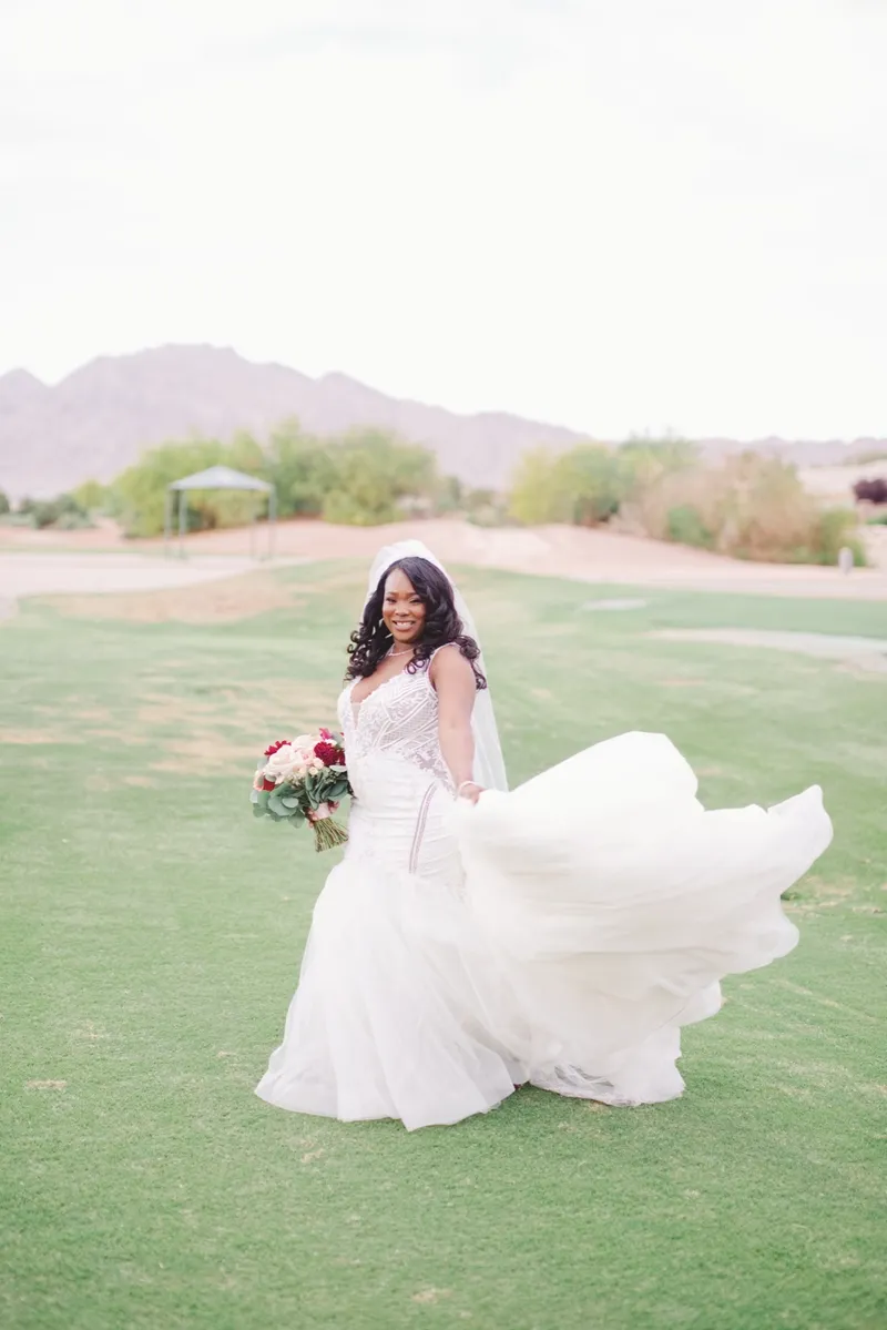 Bride sweeping her gown out across the fairway with a red bouquet in her hand and the mountains behind