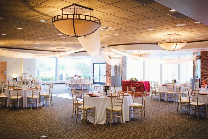 Clubhouse reception room set with round tables and gold chairs, ceiling draping gathered around a chandelier above the wood dance floor