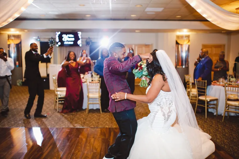 Couple dancing on the wood floor while guests watch and film from the edges of the room