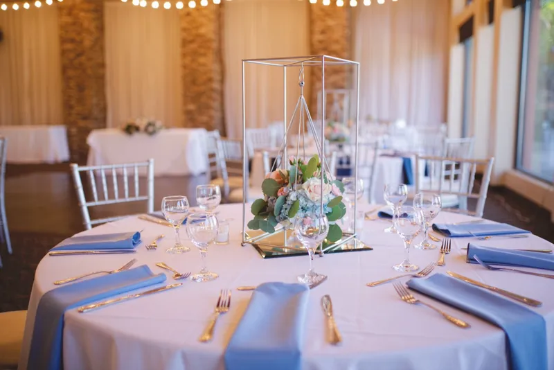 Reception table set with dusty blue napkins, gold flatware and a geometric glass centerpiece
