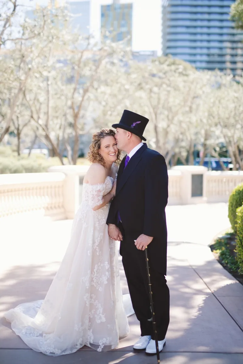 Bride resting her head against her groom, who wears a black tailcoat and top hat and holds a cane