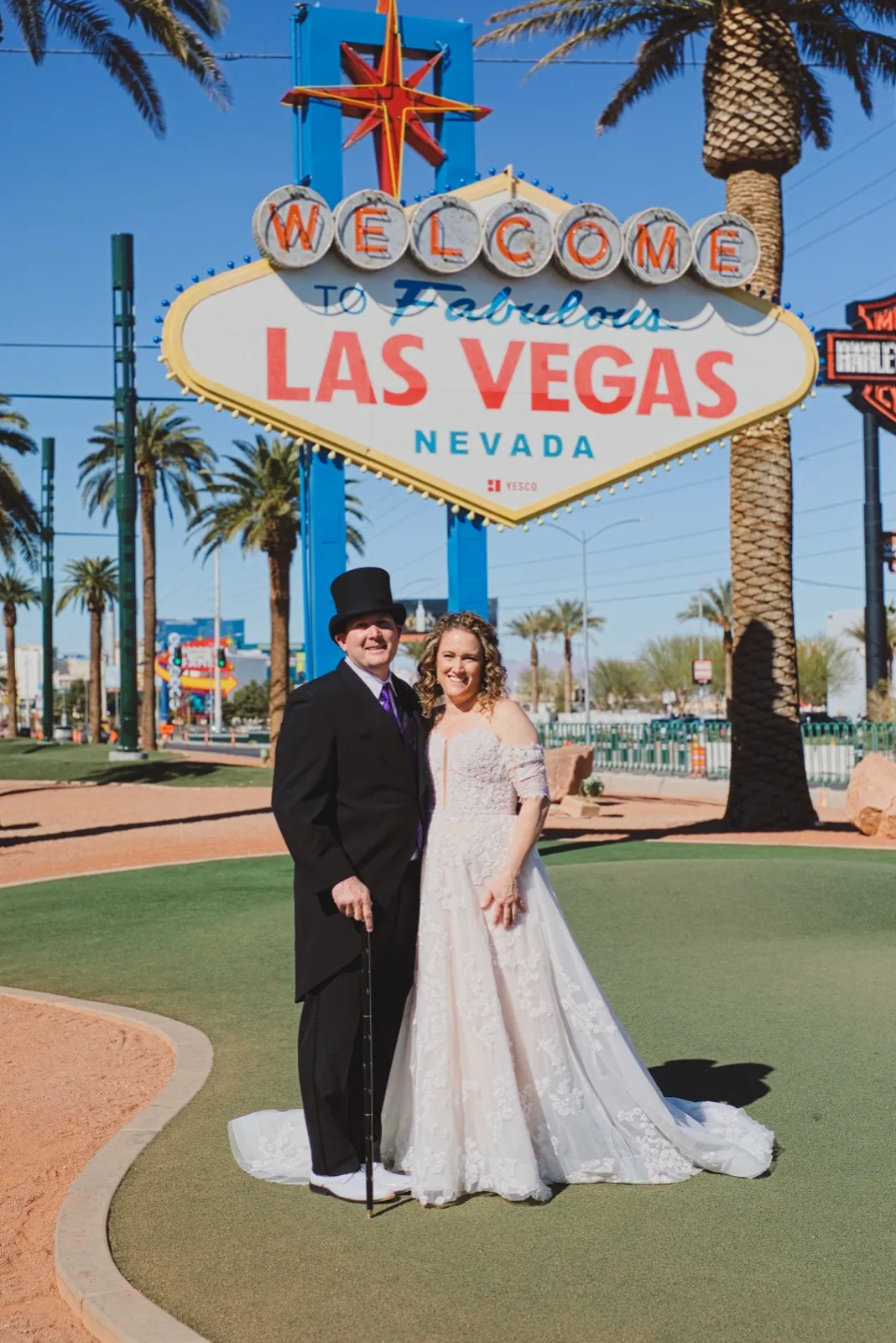 A groom in a black top hat and tails and his bride pose under the Welcome to Fabulous Las Vegas sign