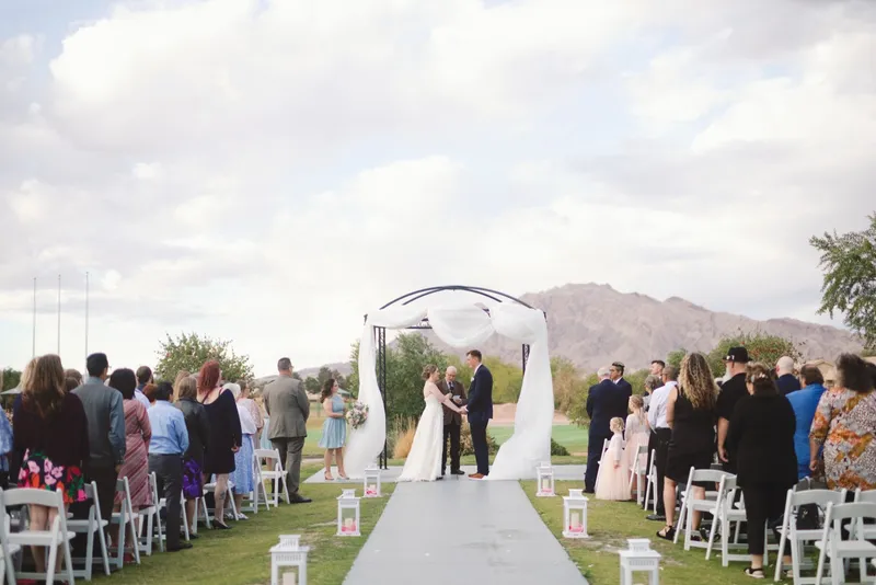 Guests standing on both sides of the aisle around the couple at the draped arch during the ceremony