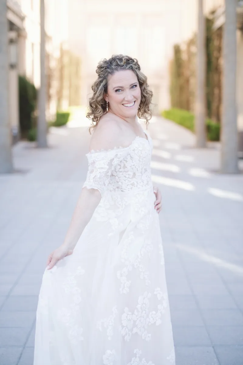Bride looking back over her shoulder and smiling while she holds the side of her lace skirt