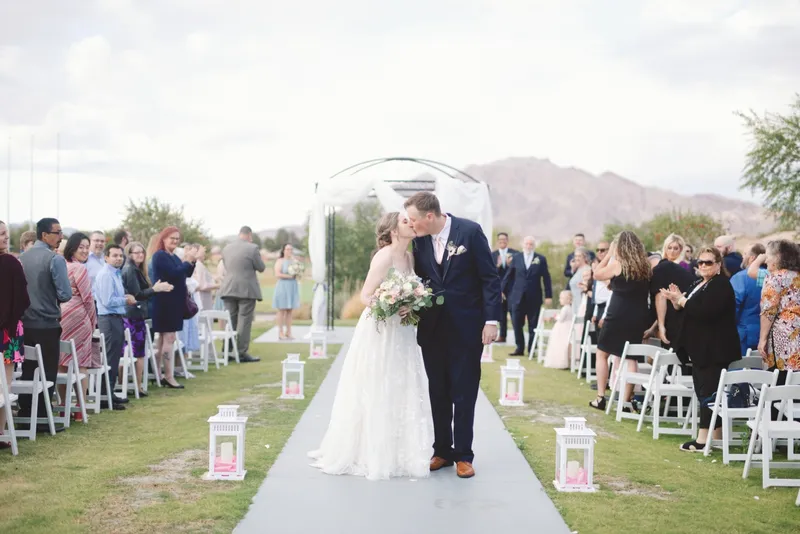 Couple kissing at the end of the aisle while guests cheer and lean in from both sides