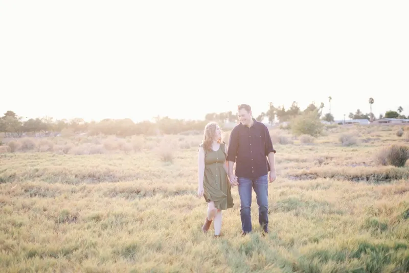 Couple walking hand in hand through a wide field of marsh grass with palm trees on the far horizon