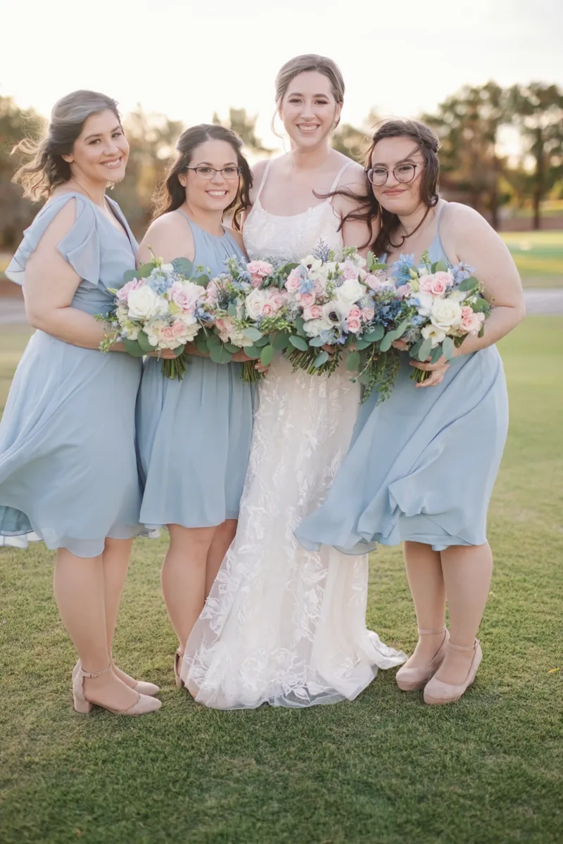 Bride standing with three bridesmaids in dusty blue dresses, all holding pastel bouquets