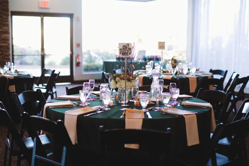 Reception tables in deep green linens with blush runners, gold candlesticks and black chairs