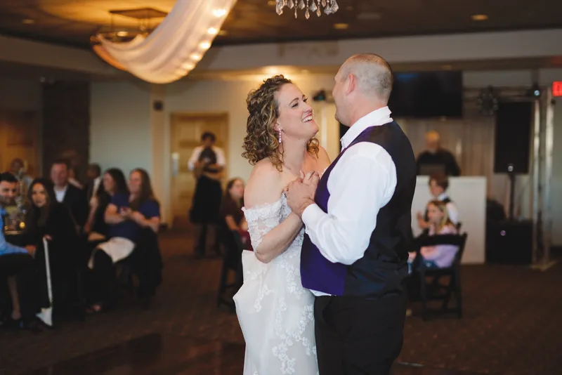Couple dancing together, the groom in his vest and shirtsleeves, guests watching from the tables