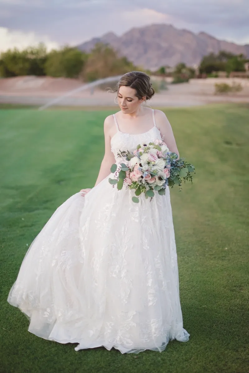 Bride standing on the fairway holding a pastel bouquet with the mountain ridge in the distance