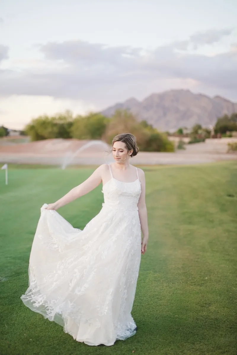 Bride swinging her lace gown out across the green in low afternoon light