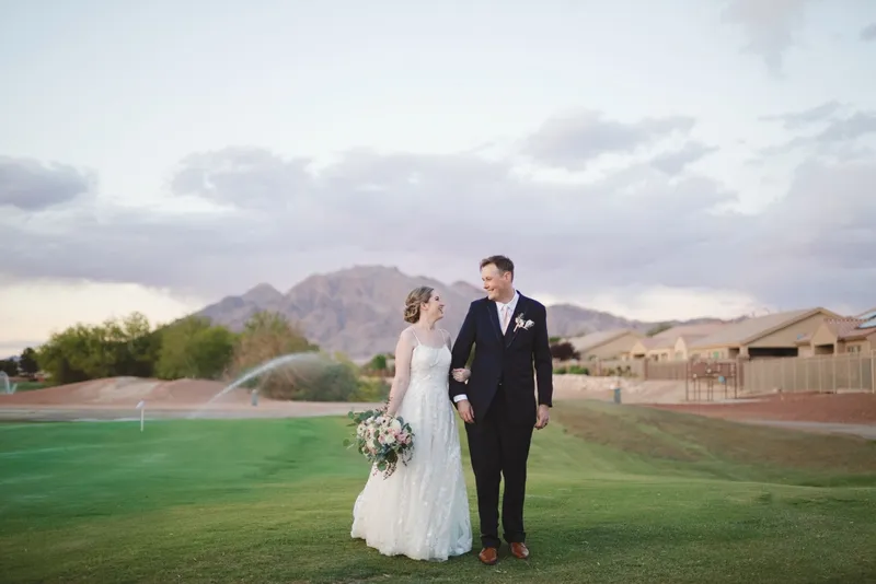 Couple standing together out on the course under a sky full of broken cloud with the mountains beyond