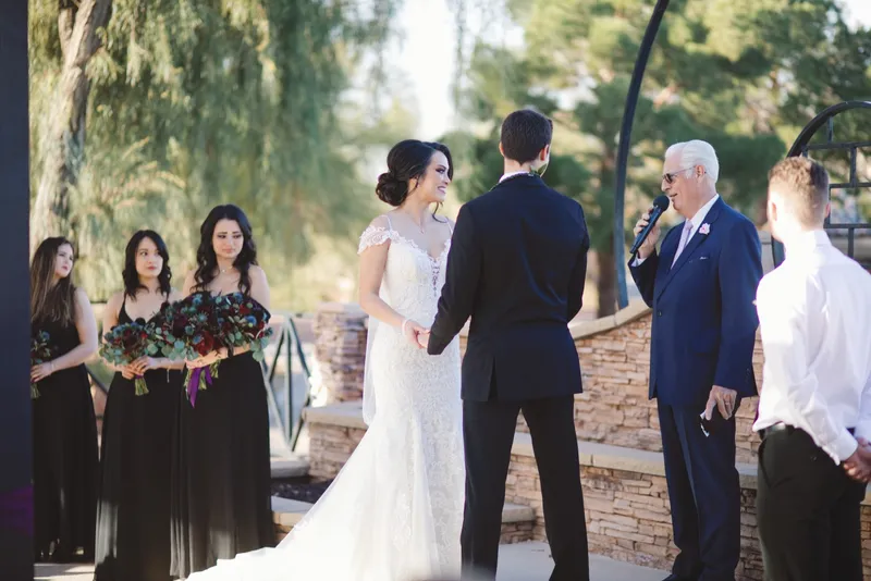 Couple holding hands through the vows with bridesmaids in black dresses standing beside them
