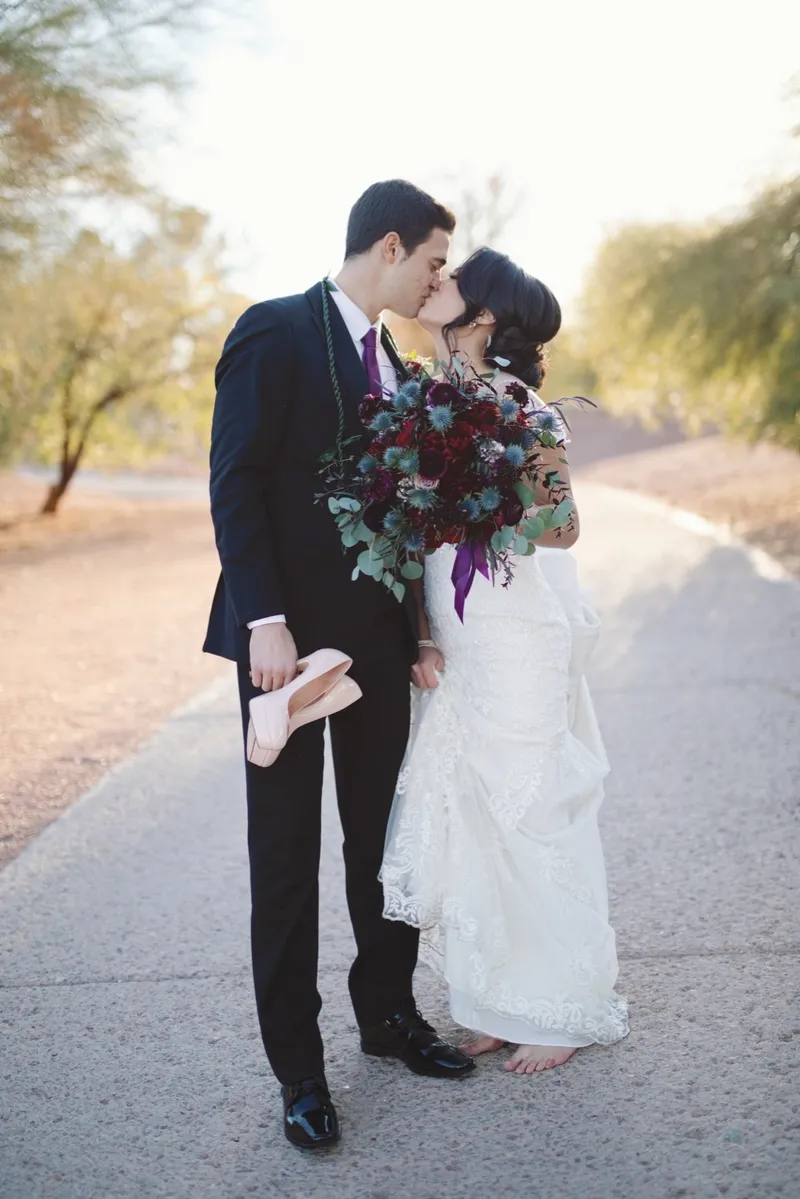 Couple kissing on the cart path with her burgundy bouquet held between them