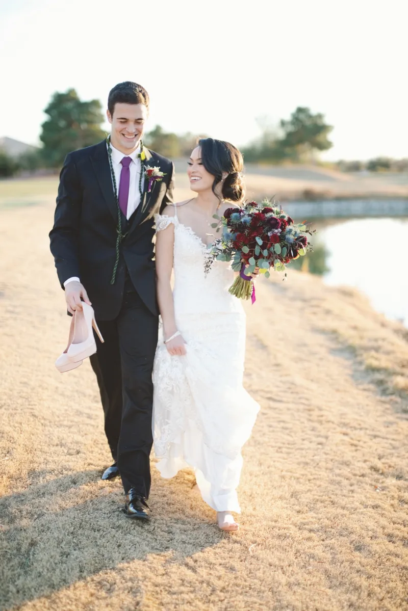 Couple walking the fairway with the groom carrying the bride's shoes and her bouquet in her hand