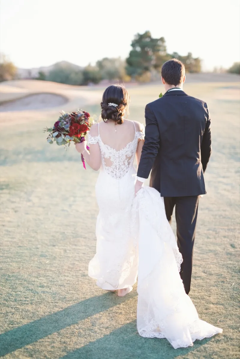 Couple walking away across the green with the bride's train trailing behind her