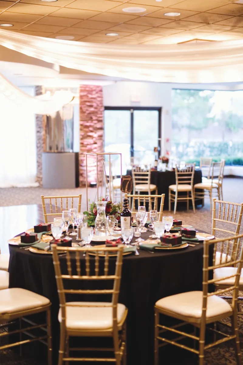 Reception tables in black linens with gold chairs and burgundy floral centerpieces