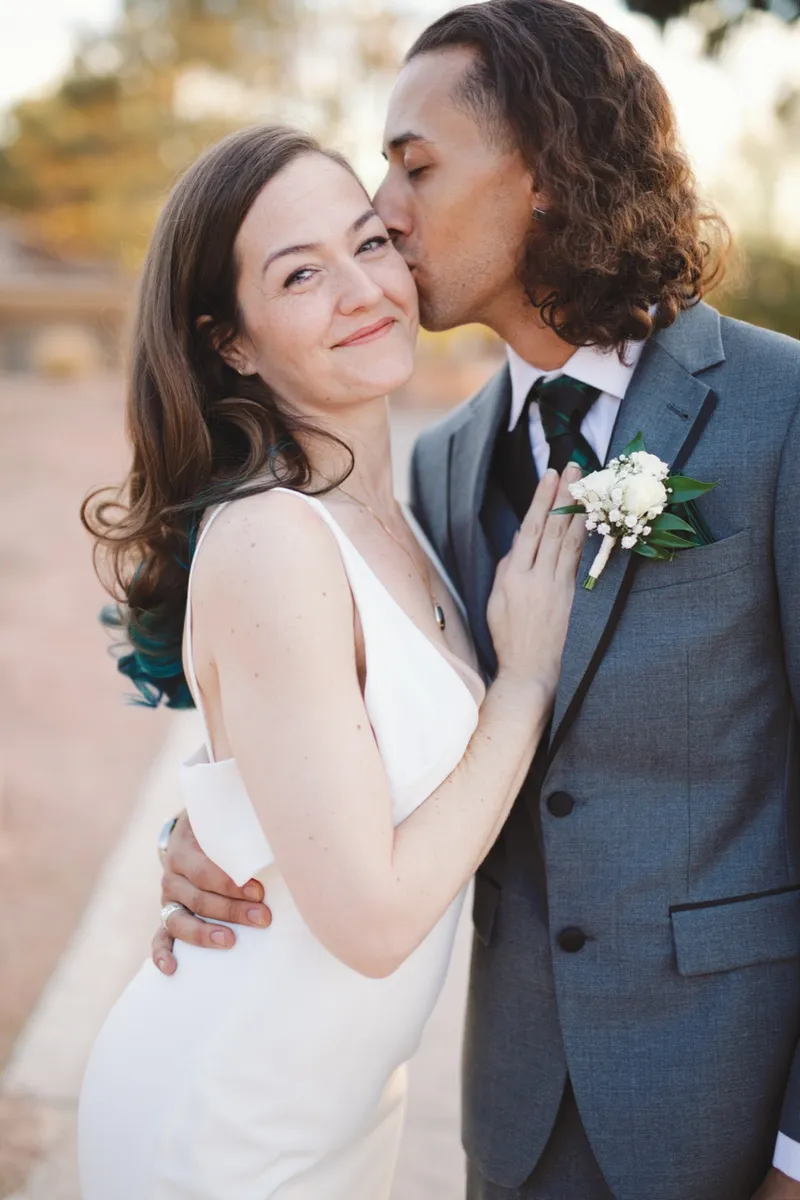 Groom kissing the top of the bride's head in a close portrait outdoors