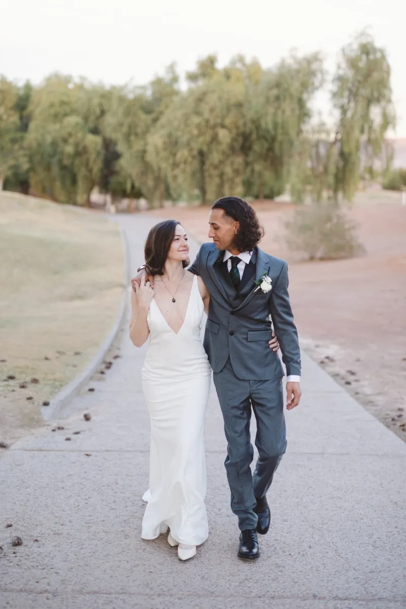 Couple walking the path together, the bride in a simple slip gown and the groom in a blue suit