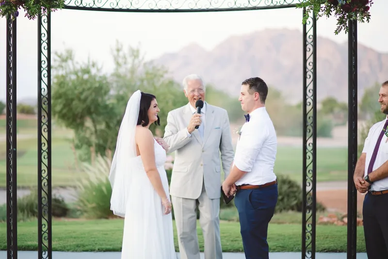 Couple and officiant framed inside the black iron rotunda with the fairway and mountains filling the opening behind them