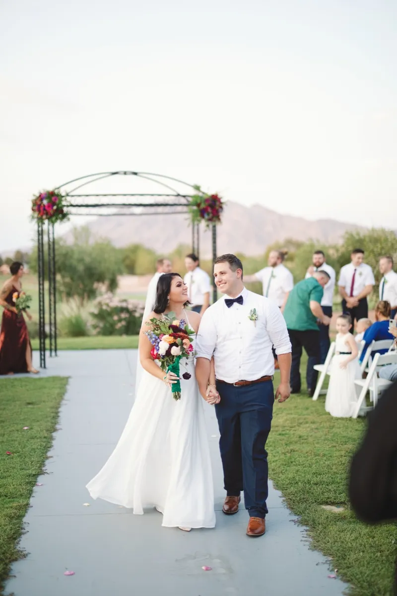 Couple coming back up the aisle together after the ceremony, the bride holding a bright bouquet of oranges and reds