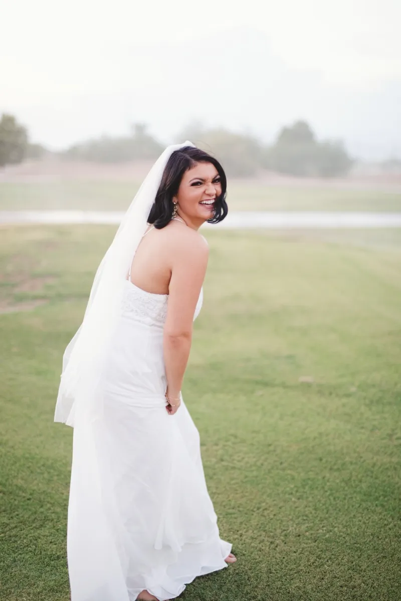 Bride looking back over her shoulder on the lawn with her veil trailing out behind her
