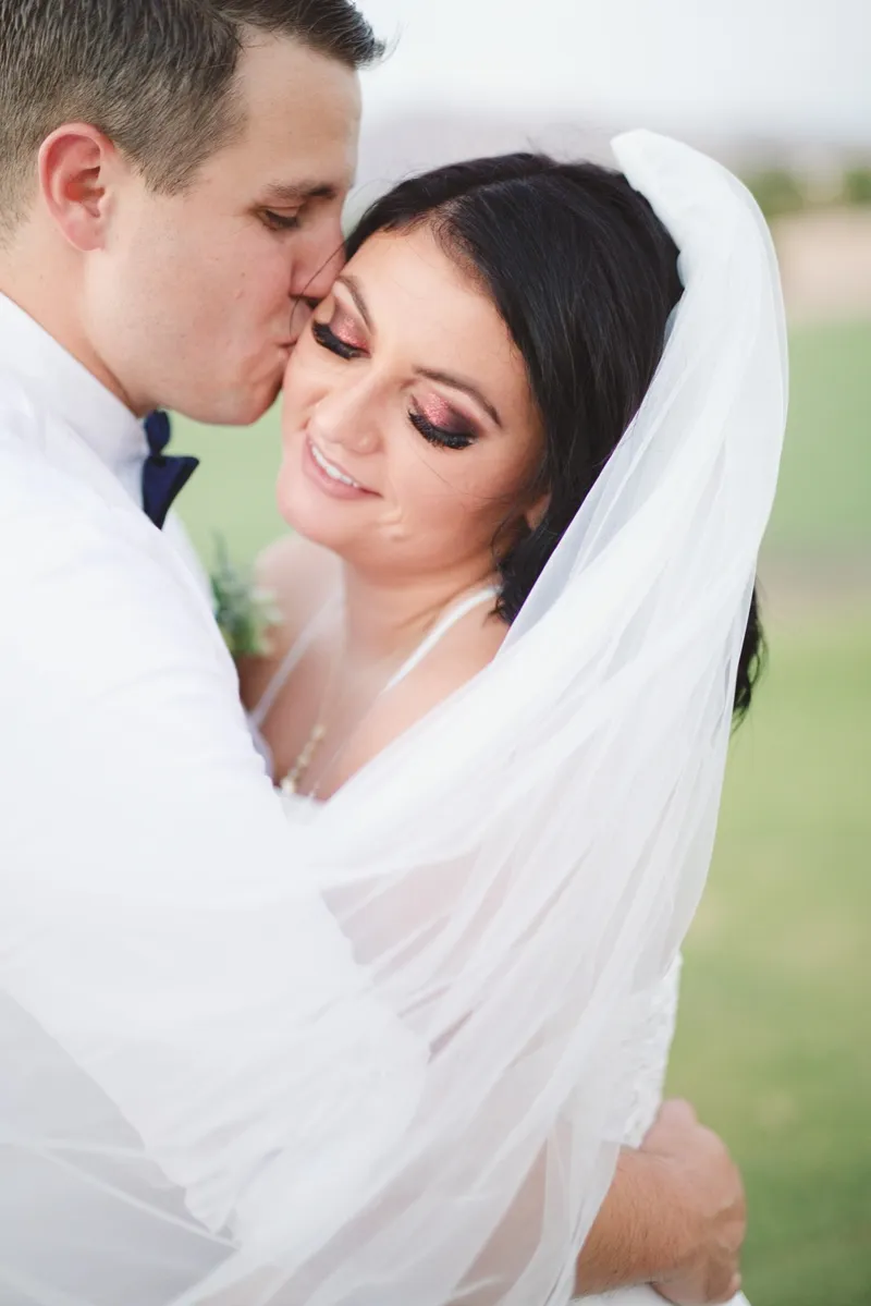 Close portrait of the groom kissing the bride's temple with her veil pulled across the frame