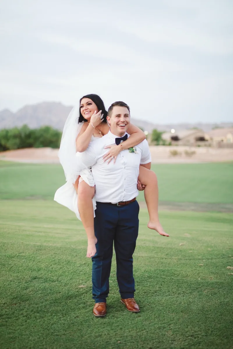 Groom giving the bride a piggyback ride across the grass, both of them laughing