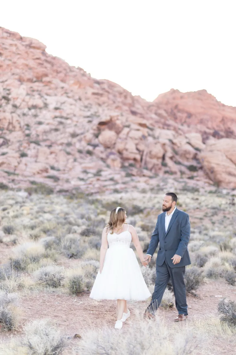Bride and groom standing together in the brush below the red rock ridge