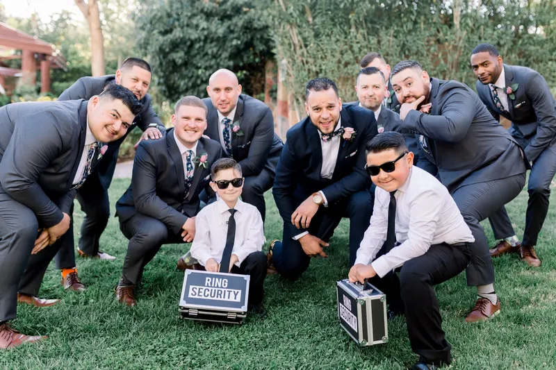 The groomsmen crouched together on the grass with the two ring bearers and their cases in the middle of the group