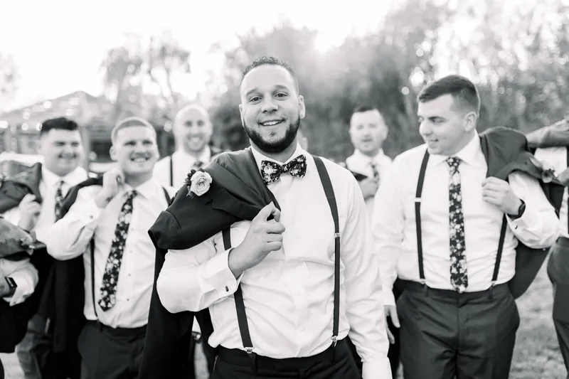 Black and white photo of the groomsmen piling onto each other and laughing on the grass
