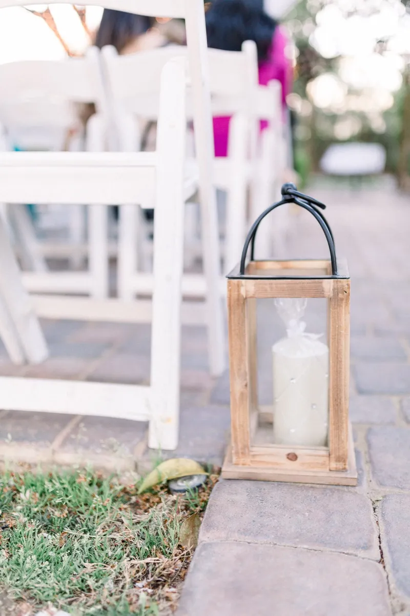 A wooden candle lantern set on the paver aisle beside the front row of white ceremony chairs