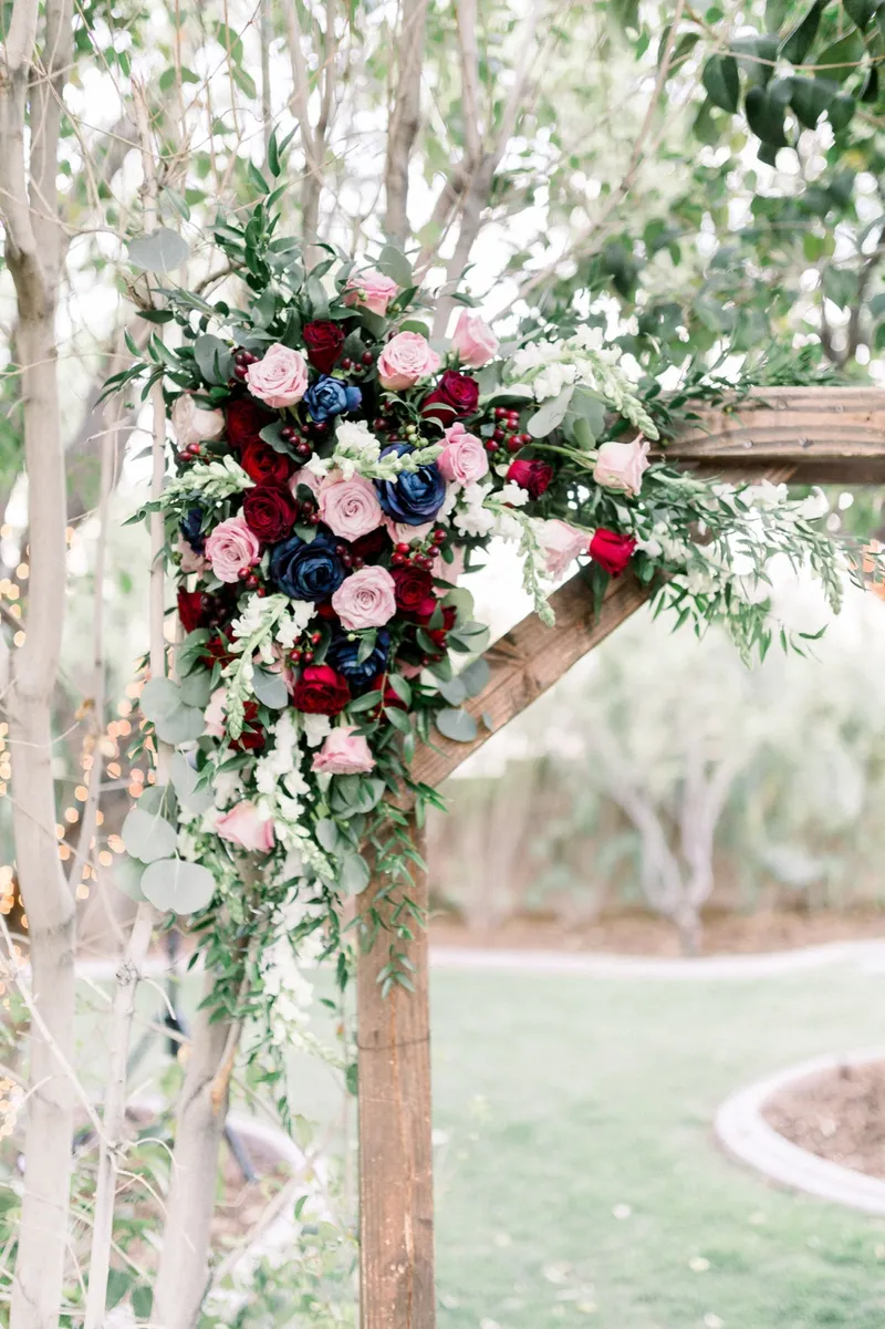 Close view of the burgundy, navy and blush rose arrangement mounted on the corner post of the wooden arbor
