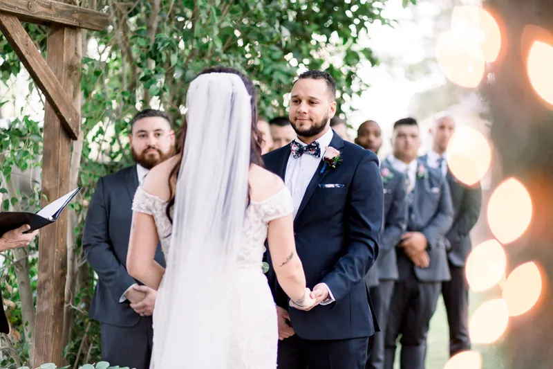 The bride and groom standing close at the arbor during the ceremony with her veil hanging behind them