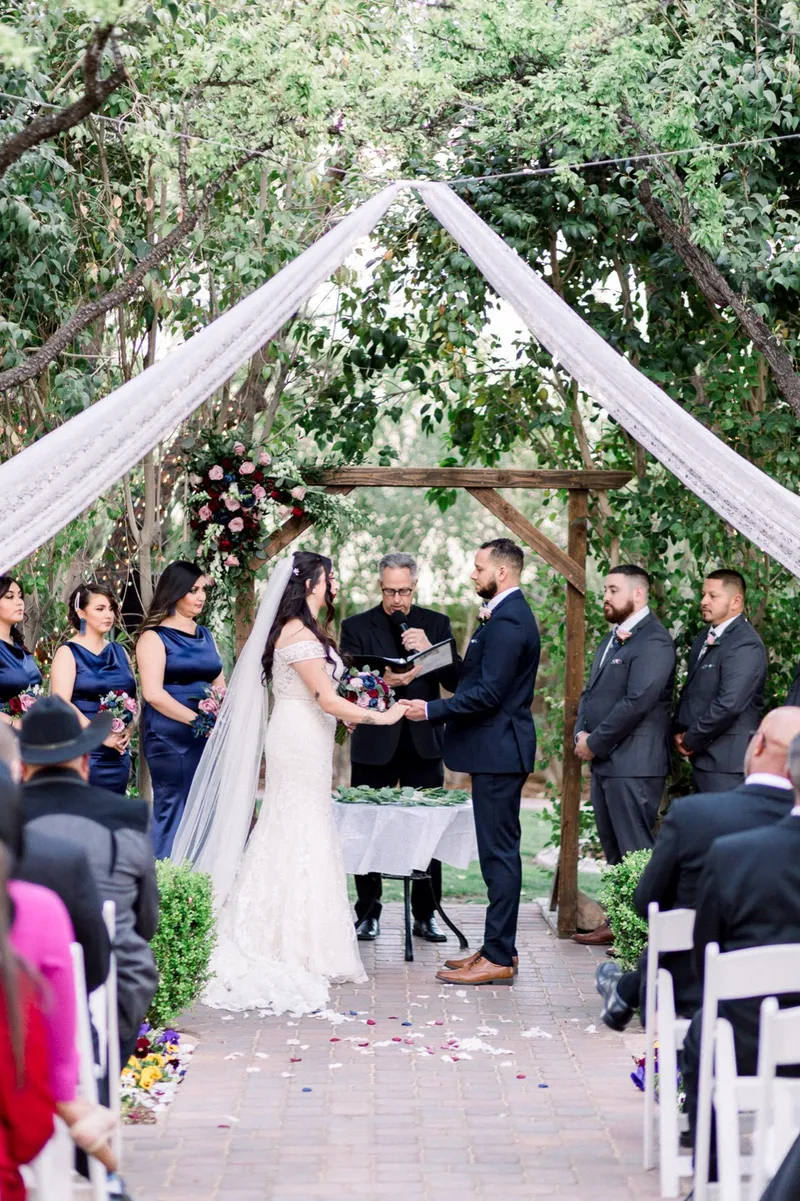 The couple holding both hands in front of the officiant under the floral wooden arbor