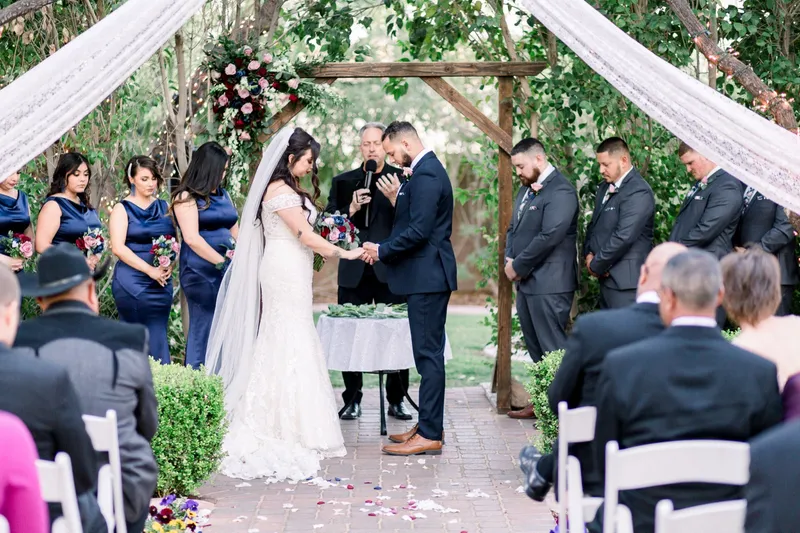 The couple at the arbor with bridesmaids in navy on one side and groomsmen in grey suits on the other