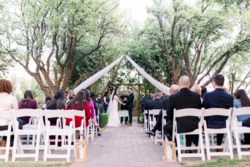 View down the aisle over rows of seated guests toward the bride and groom standing together at the arbor