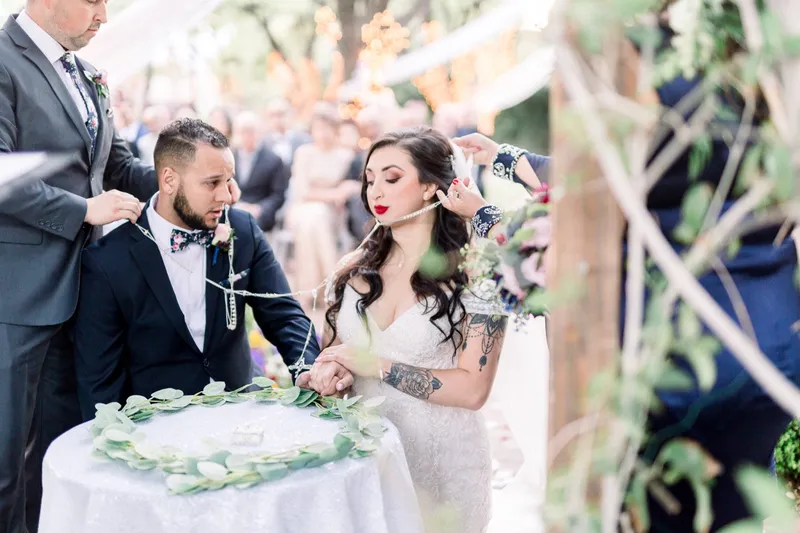 The bride and groom standing joined by the beaded lazo at the eucalyptus ringed table during the ceremony