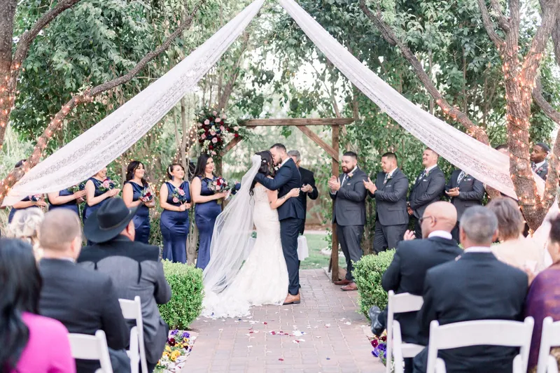 The bride and groom kissing at the end of the aisle with the wedding party and guests watching from their chairs