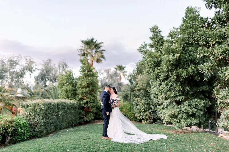 The bride and groom standing forehead to forehead on the lawn with her veil train spread out on the grass