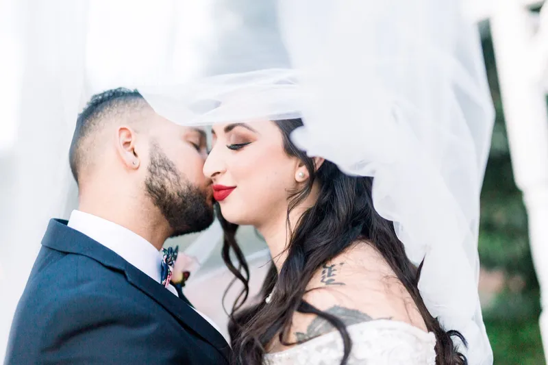 Close portrait of the groom kissing the bride's cheek beneath her veil, her eyes closed