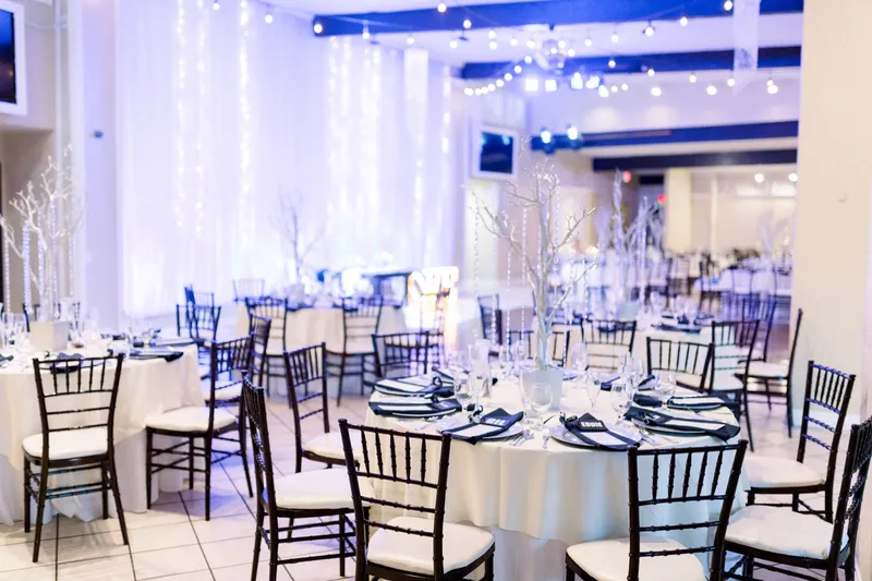 The indoor reception room set with round tables and dark chiavari chairs in front of a twinkle light backdrop under blue uplighting