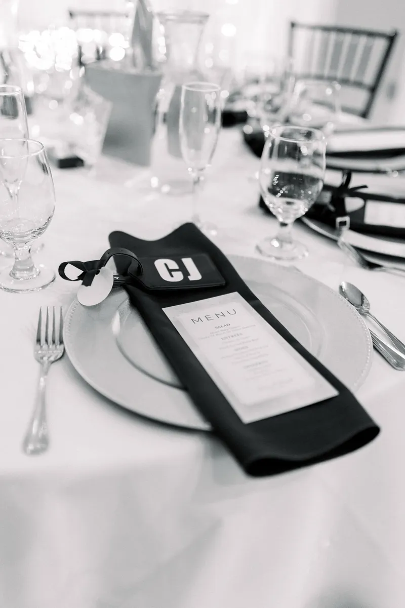 Black and white close view of a place setting with a menu card and a monogrammed napkin tag